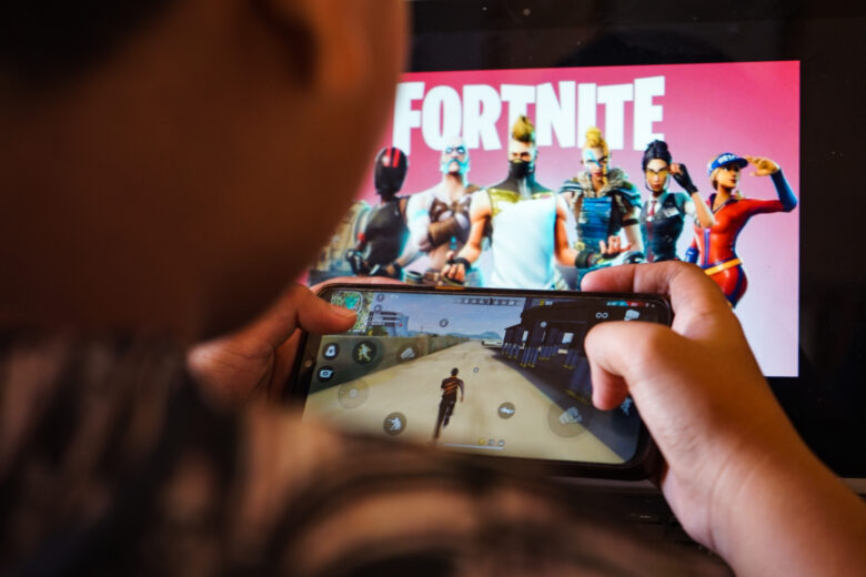 August 15, 2020, Makassar, South Sulawesi, Indonesia: A child is playing a game on a cellphone with a picture of the Fortnite game on the computer screen in the background. Apple and Google announced their decision to remove Fortnite games from the App Store and Google Play app stores. (Credit Image: © Herwin Bahar/ZUMA Wire)